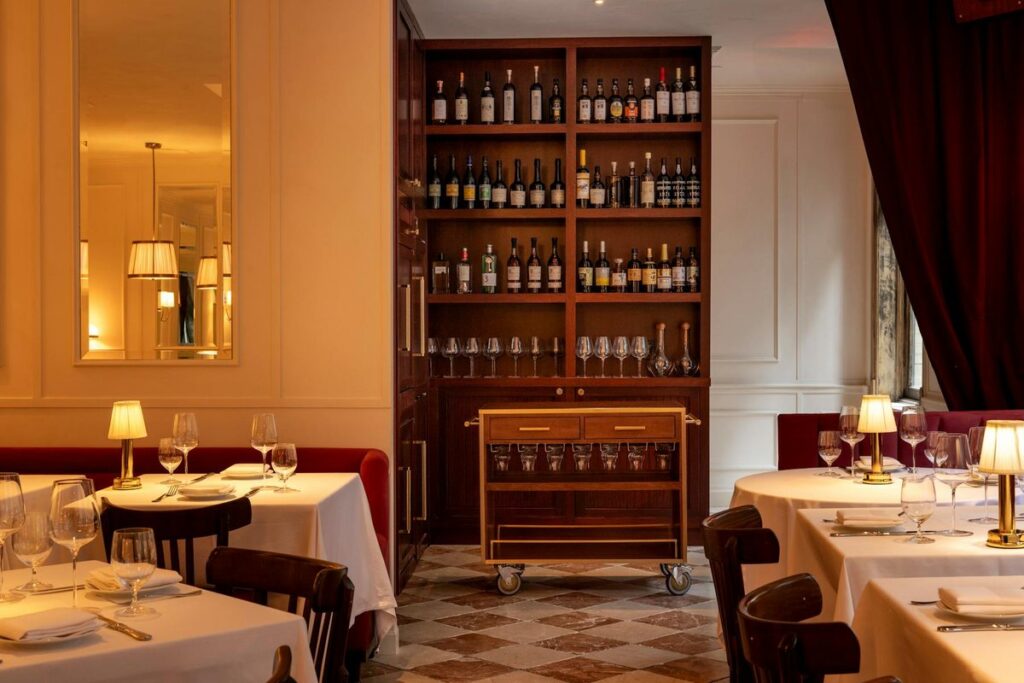 The wine cabinet and a brass bar cart between candlelit tables at Chateau Royale