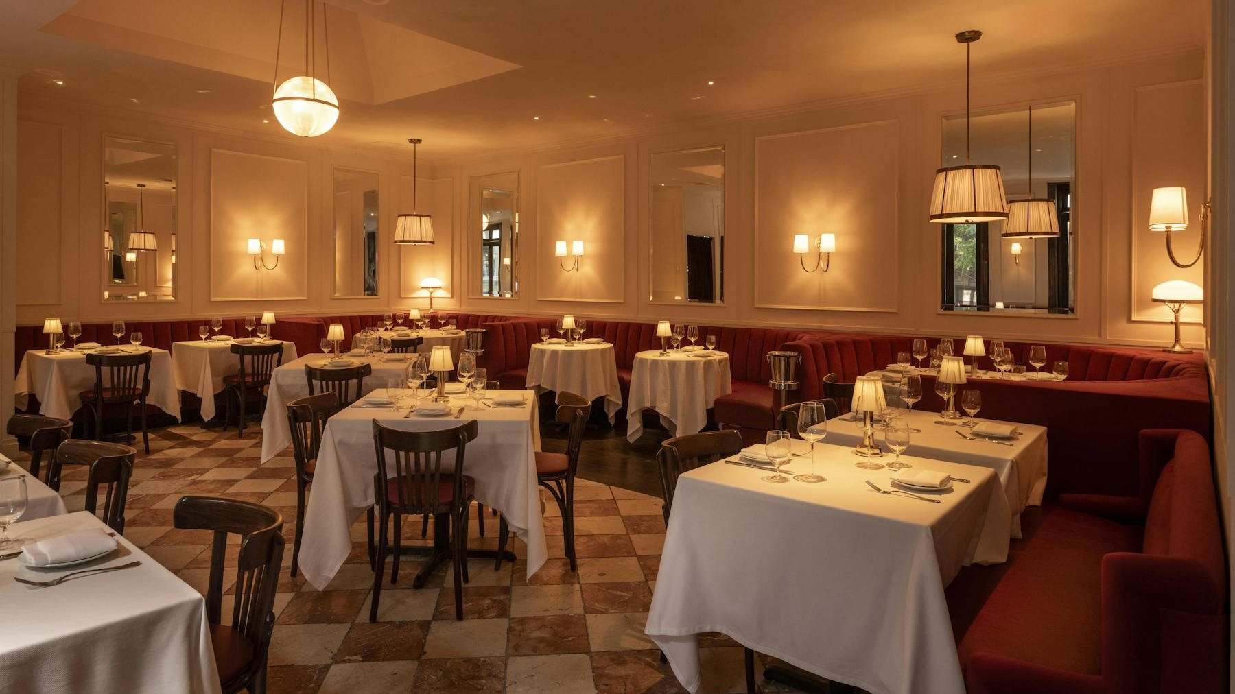 Chateau Royale's Dining Room with white tablecloths, red banquettes, wall sconces and a checkerboard floor